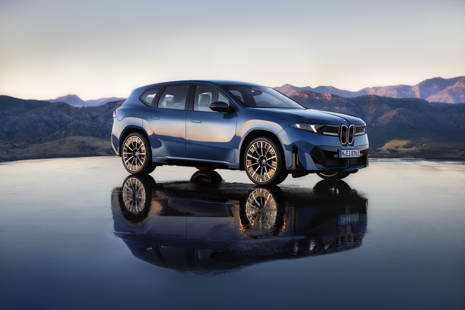 SUV eléctrico BMW iX3 azul estacionado con montañas detrás, vista frontal de tres cuartos