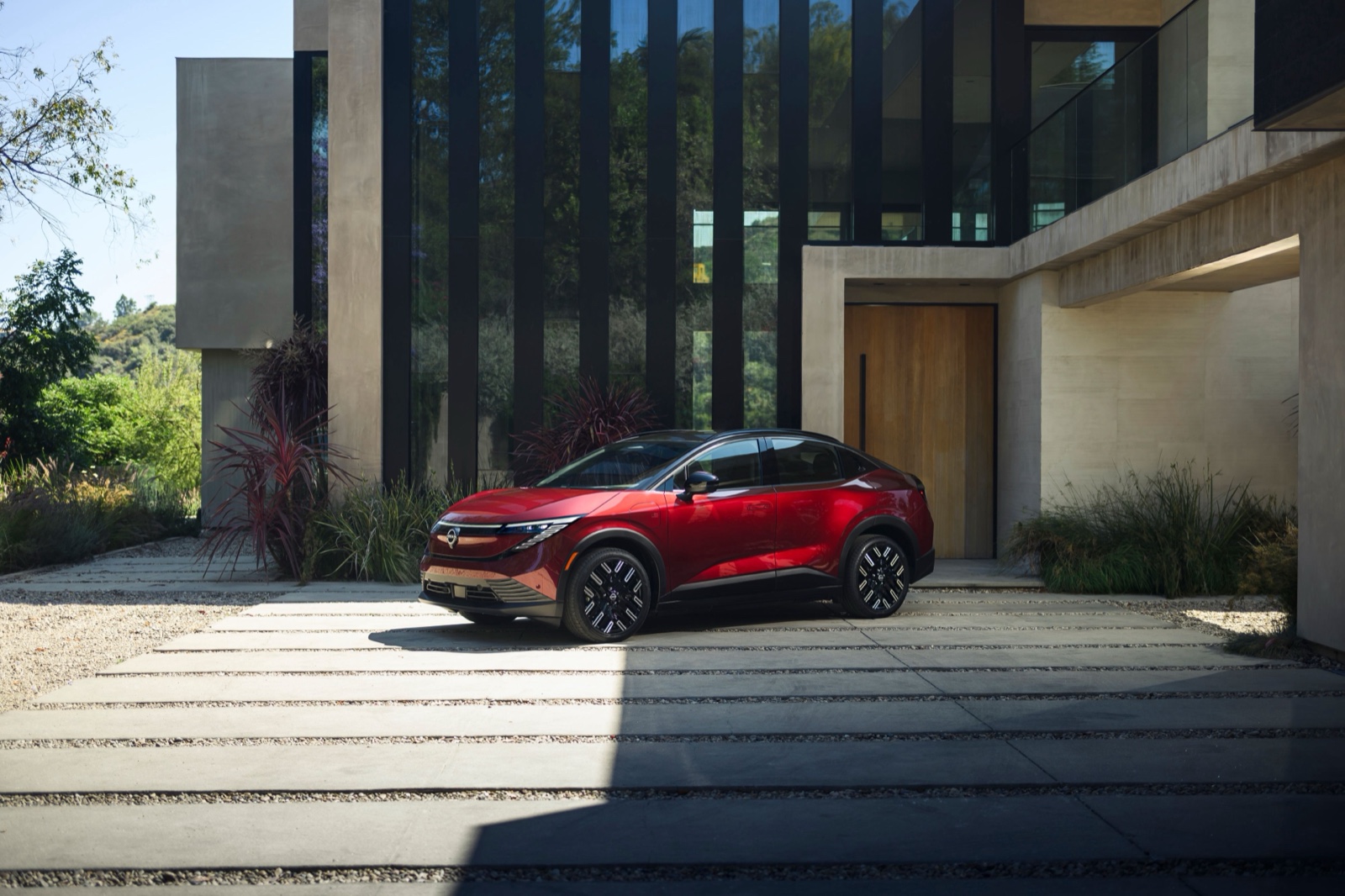 Nissan Leaf rojo 2026 estacionado afuera de una casa moderna, vista frontal de tres cuartos